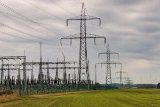 Ηλεκτρικό δίκτυο υψηλής τάσης με πυλώνες και ανεμογεννήτριες στο βάθος σε γερμανικό τοπίο