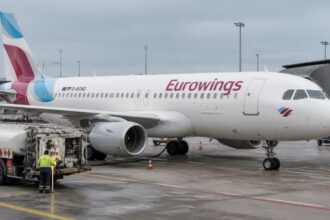 Αεροσκάφος της Eurowings σε αεροδρόμιο, με όχημα ανεφοδιασμού και εργαζόμενο εδάφους δίπλα του.