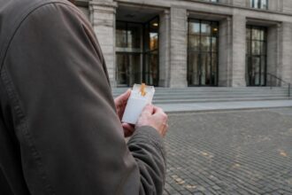 Άνδρας κρατά πακέτο τσιγάρα μπροστά από κτίριο δικαστηρίου στη Γερμανία.