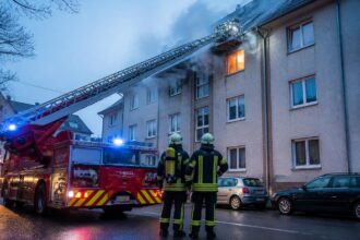 Πυροσβεστικό κλιμακοφόρο όχημα και πυροσβέστες μπροστά σε πολυκατοικία με καπνό, σε συμβολική εικόνα