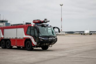 Πυροσβεστικό όχημα αεροδρομίου σε χώρο στάθμευσης αεροσκαφών με επιβατικό αεροπλάνο στο βάθος