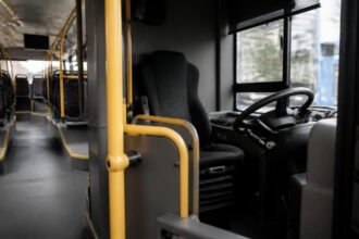 Άδεια θέση οδηγού και τιμόνι στο εσωτερικό λεωφορείου, με τις θέσεις επιβατών στο βάθος.